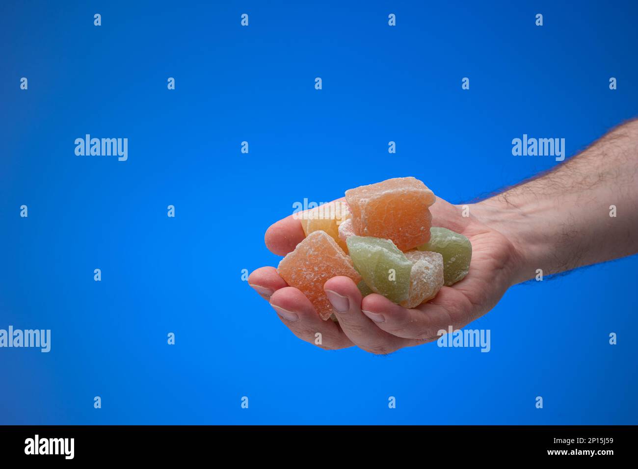 Cubetti di delizia turca colorata tenuti in mano maschile. Primo piano ripresa in studio, isolata su sfondo blu. Foto Stock