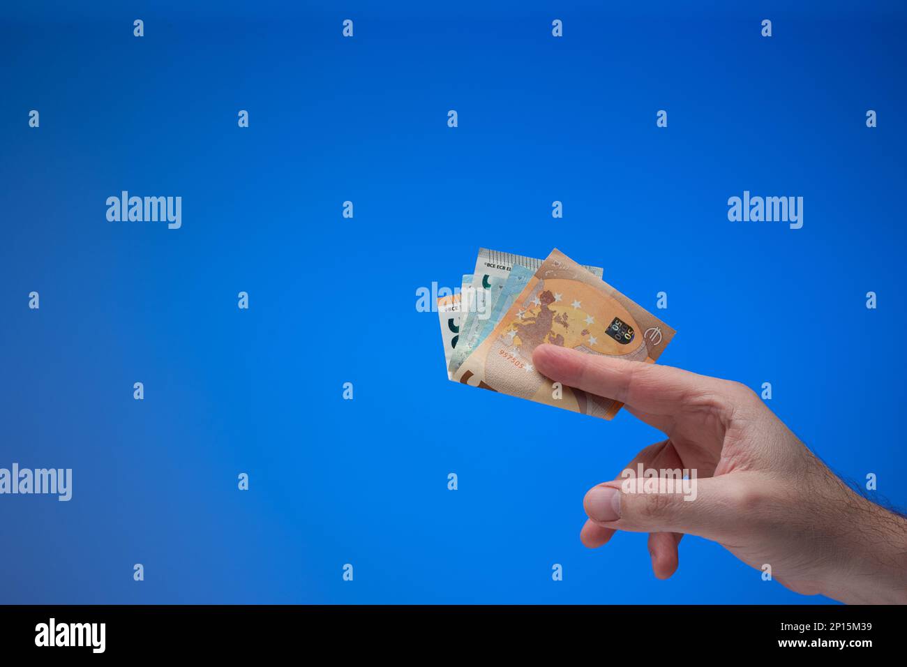 Banconote in euro in mano maschile. Primo piano ripresa in studio, isolata su sfondo blu. Foto Stock