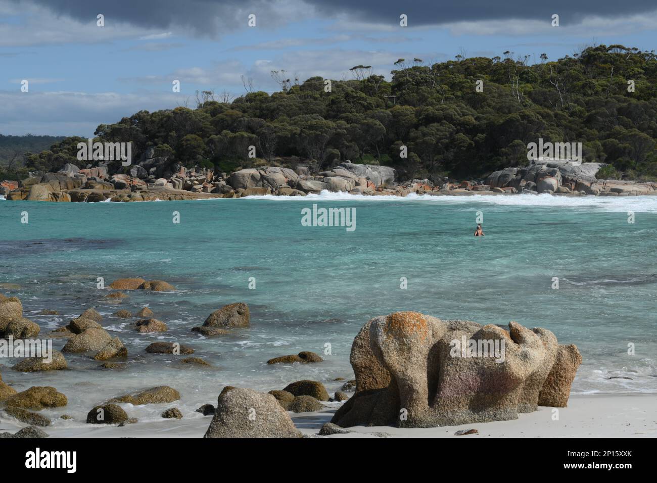 La spiaggia e i massi circostanti sono evidenziati su un mare blu con sabbia bianca e rocce scolpite Foto Stock