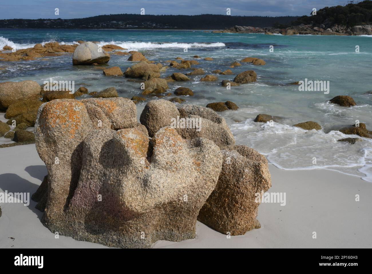 La spiaggia e i massi circostanti sono evidenziati su un mare blu con sabbia bianca e rocce scolpite Foto Stock