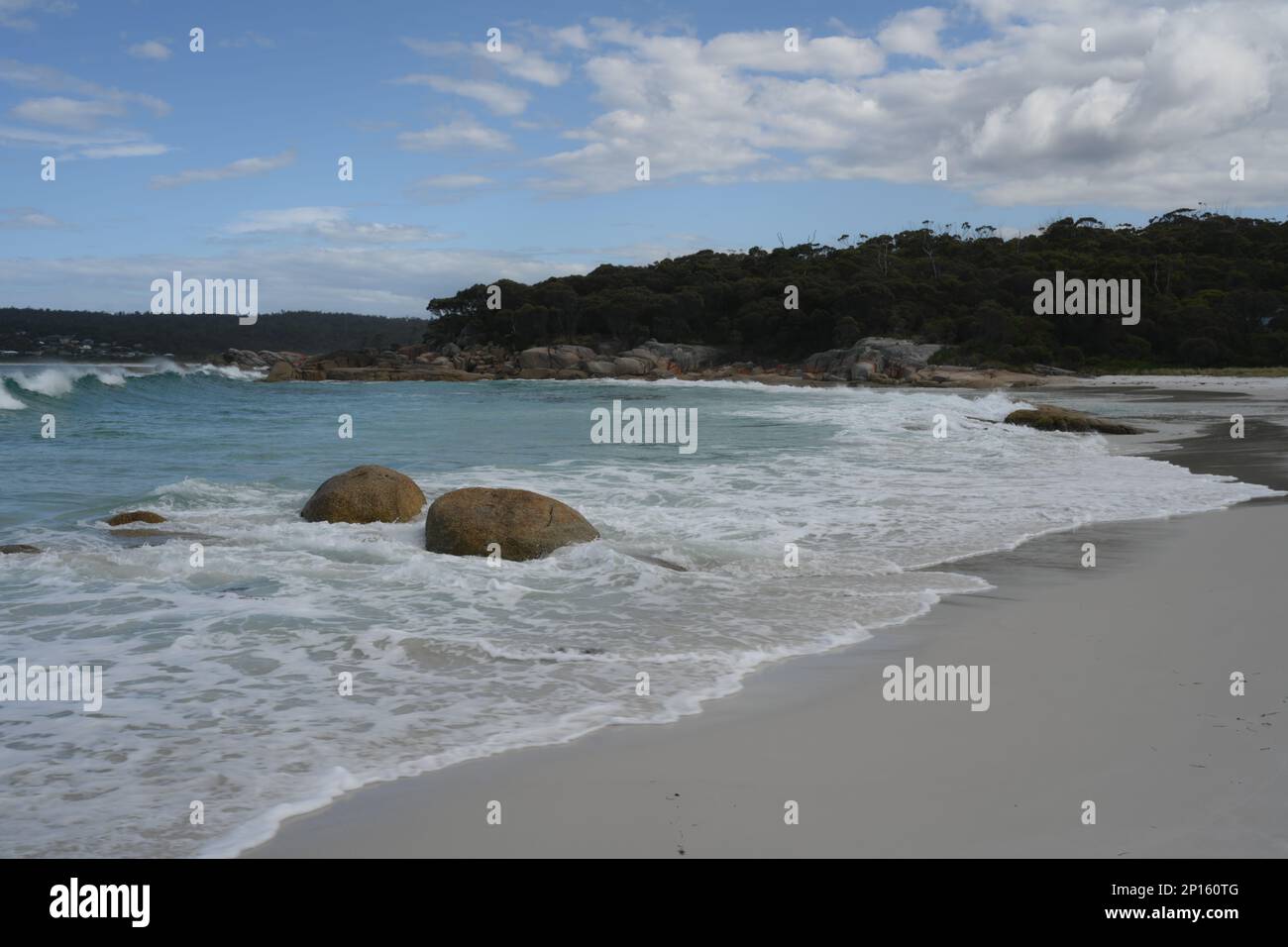 La spiaggia e i massi circostanti sono evidenziati su un mare blu con sabbia bianca e rocce scolpite Foto Stock