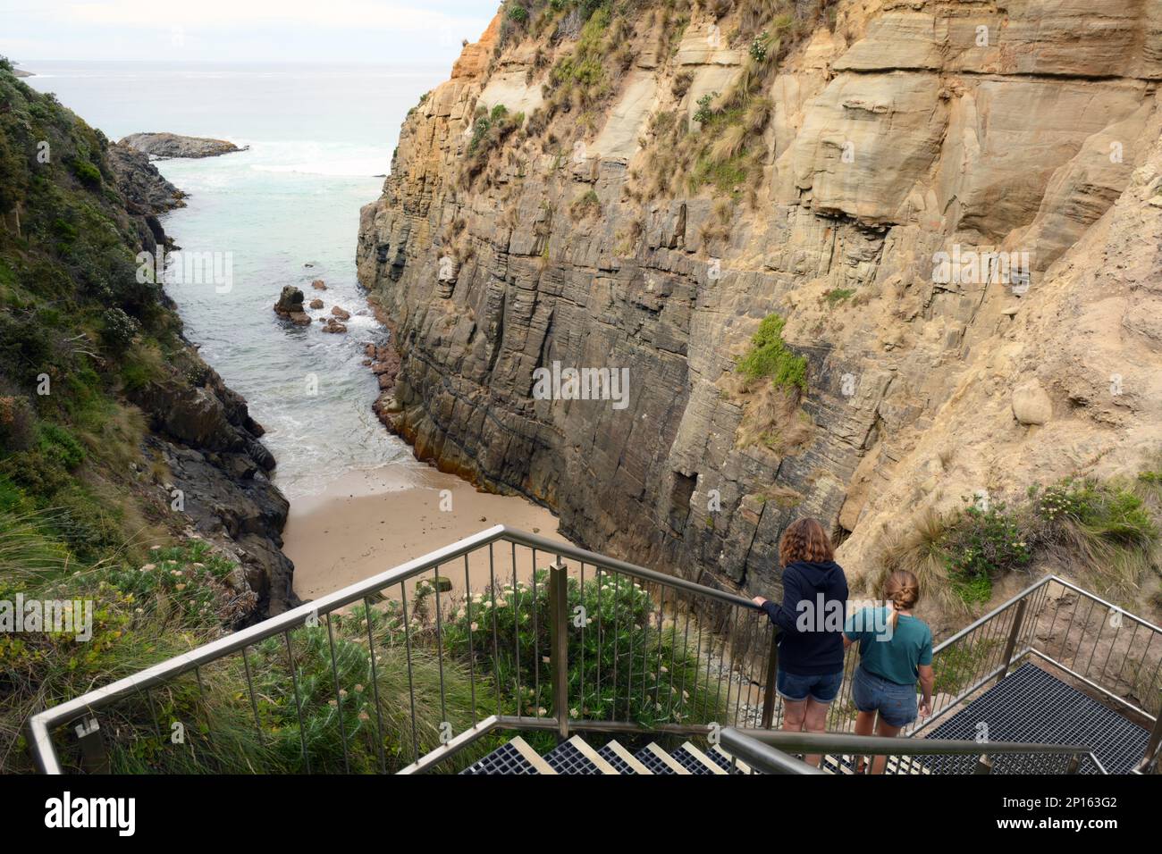 Due persone vedono le grotte notevoli dalle scale sopra il divario e il divario e. Le faglie di roccia sono state scavate dalle onde forti. Foto Stock