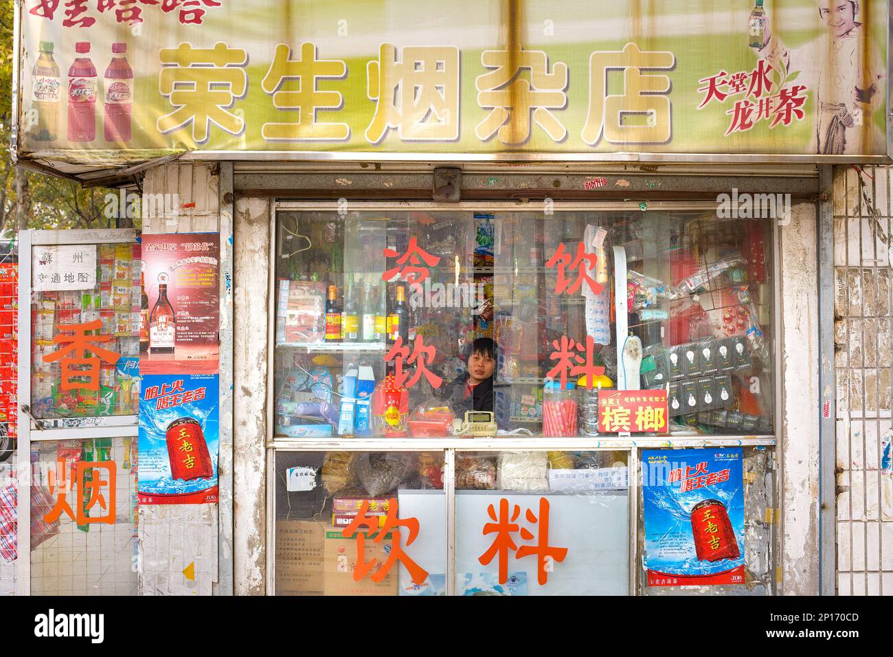 Suzhou, Provincia di Jiangsu, Cina, Una donna all'interno di un chiosco di cibo di strada con e assortimento di merci. Foto Stock