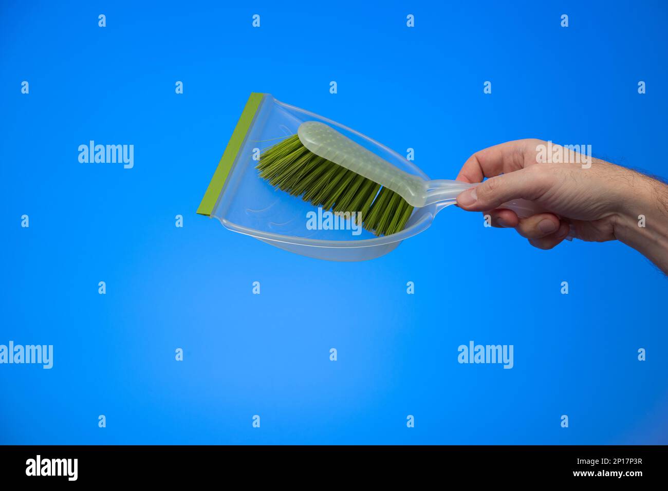 Mano maschio caucasica che tiene una spazzola di plastica verde isolato su sfondo blu studio shot. Foto Stock