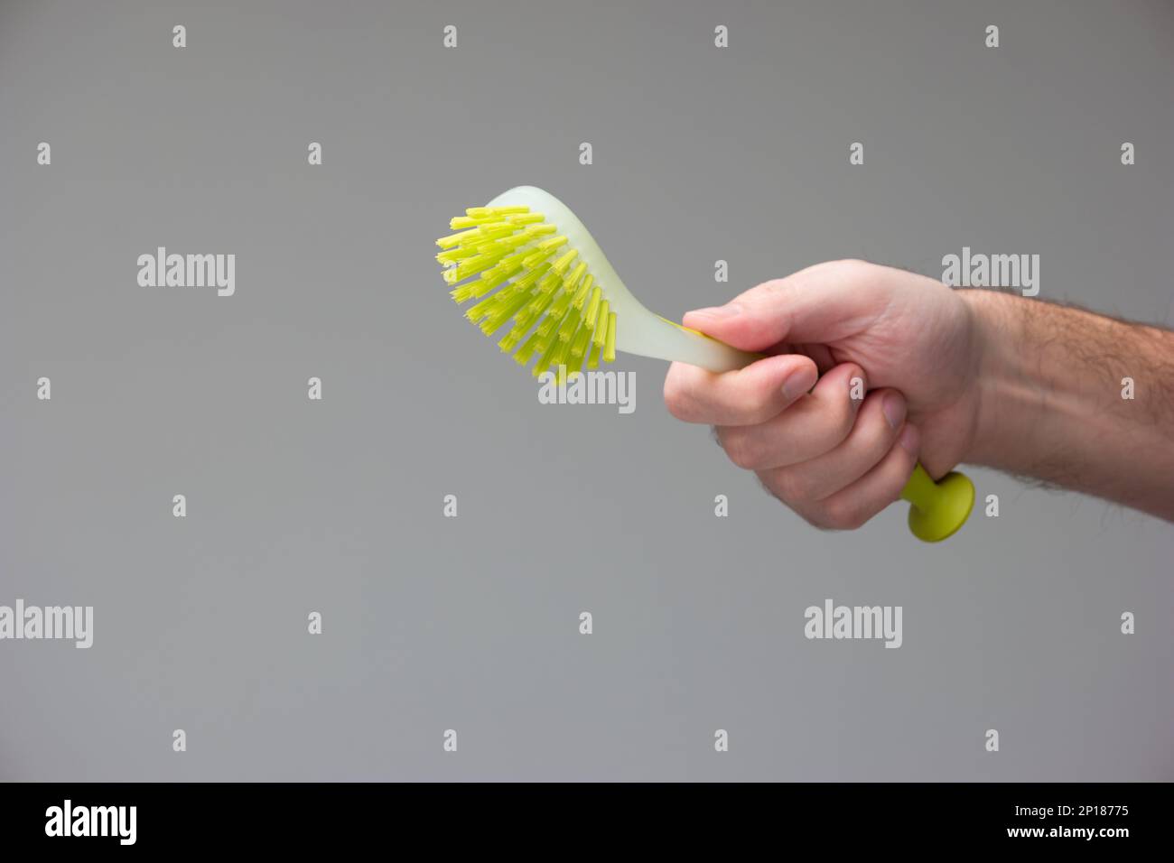 Spazzola di plastica verde in gomma per la pulizia della cucina tenuta in mano da mano maschio caucasica isolato su sfondo grigio. Foto Stock