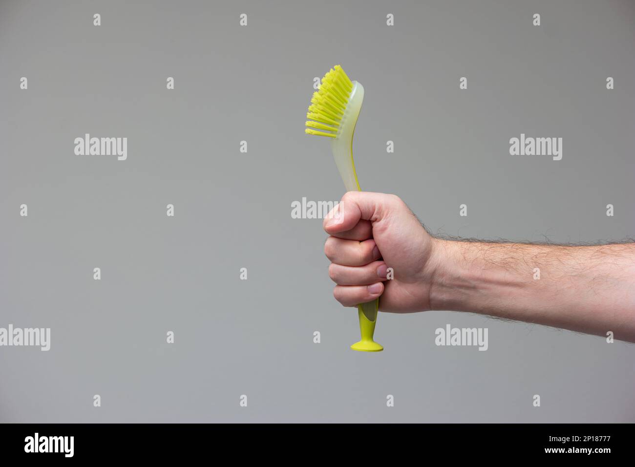 Spazzola di plastica verde in gomma per la pulizia della cucina tenuta in mano da mano maschio caucasica isolato su sfondo grigio. Foto Stock