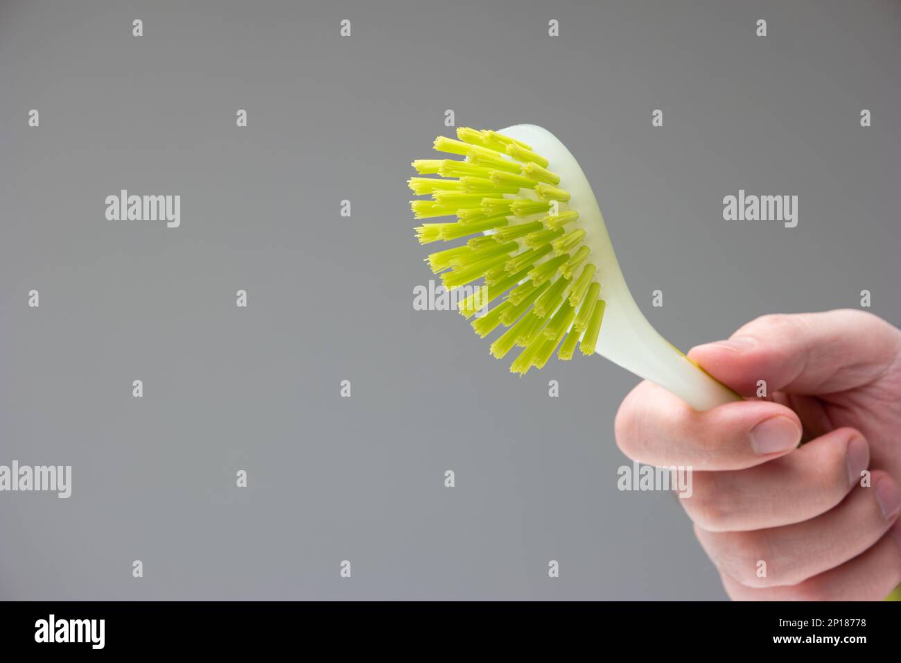 Spazzola di plastica verde in gomma per la pulizia della cucina tenuta in mano da mano maschio caucasica isolato su sfondo grigio. Foto Stock