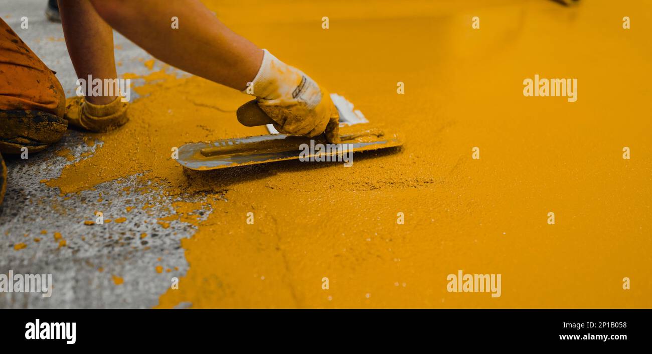 Operai edili professionisti che applicano vernice per pavimenti o un nuovo strato per un pavimento con rivestimento epossidico Foto Stock