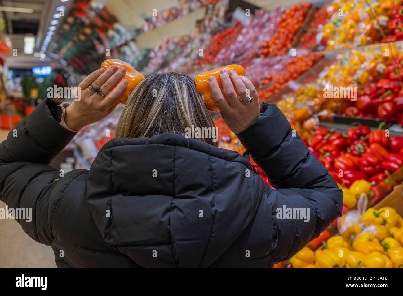 Vista divertente della donna imbrogliante con paprika arancione nel reparto del supermercato delle verdure. Svezia. Foto Stock
