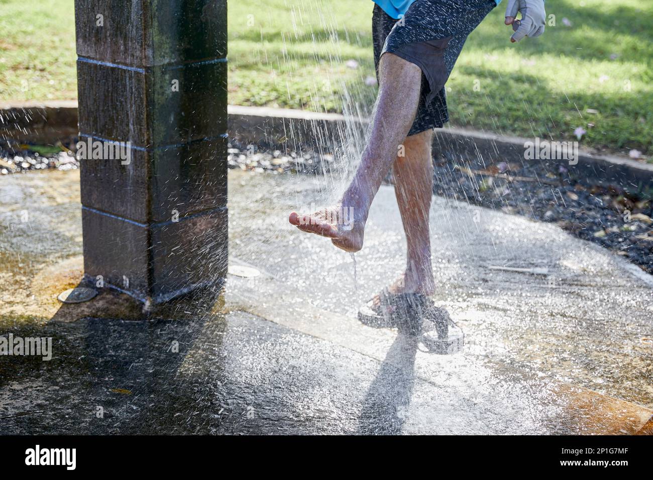 Un uomo adulto che si sciacquava i piedi alla doccia in un parco pubblico sulla spiaggia Foto Stock