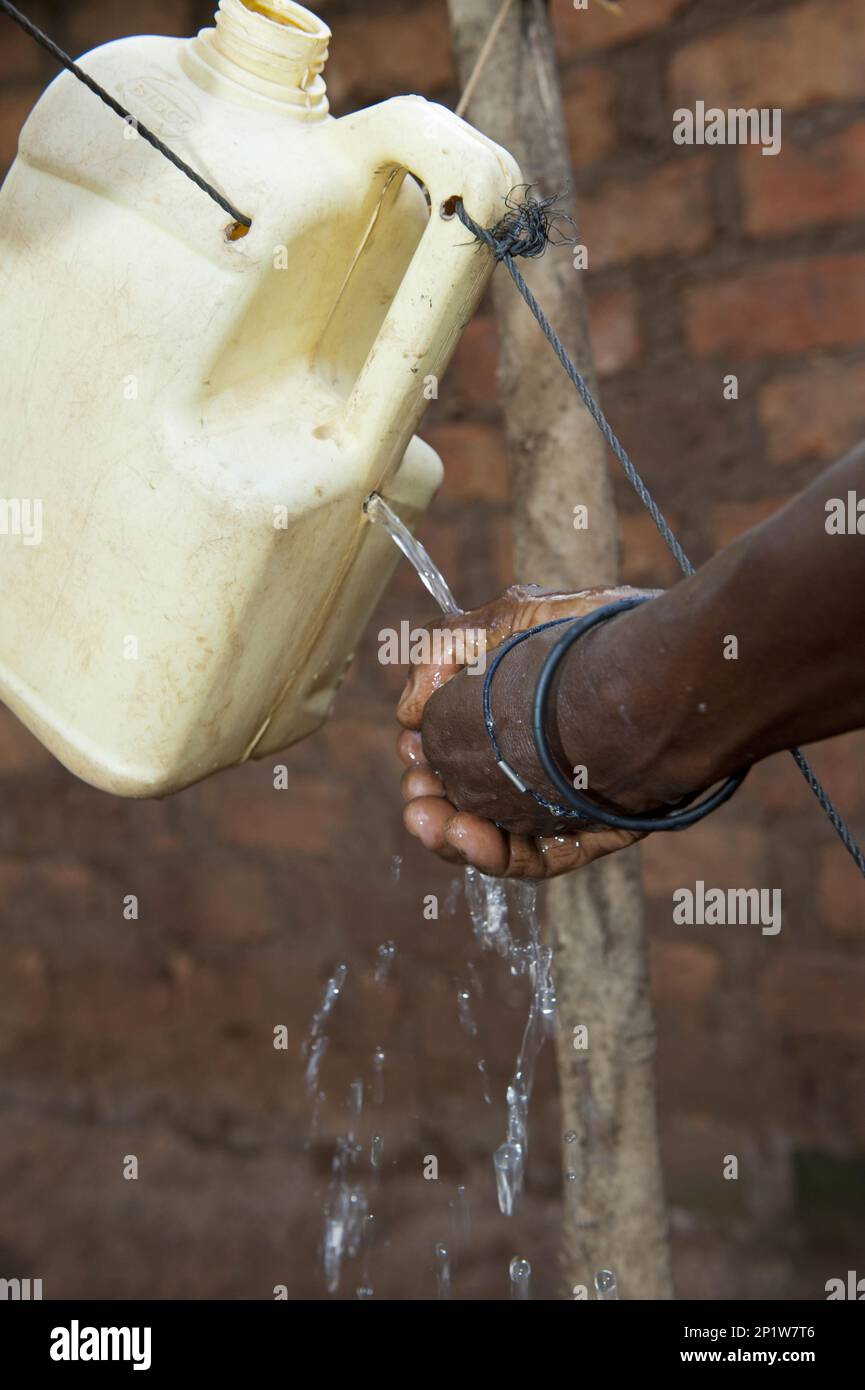 Donna lavano le mani sotto il rubinetto fatto in casa, modo efficiente per pulire le mani senza sprecare acqua, Uganda Foto Stock