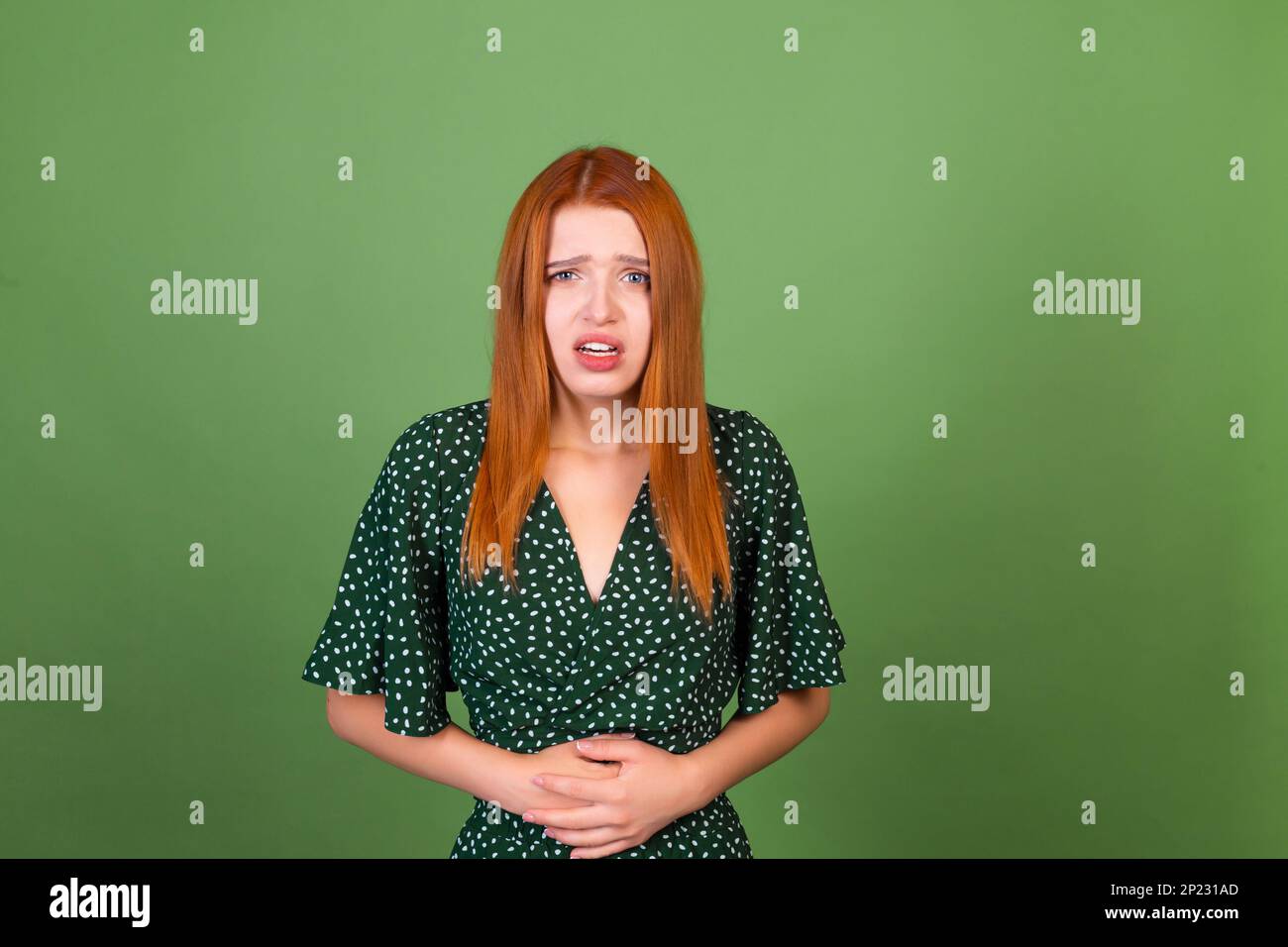 Giovane donna capelli rossi su sfondo verde triste che soffre di mal di stomaco Foto Stock