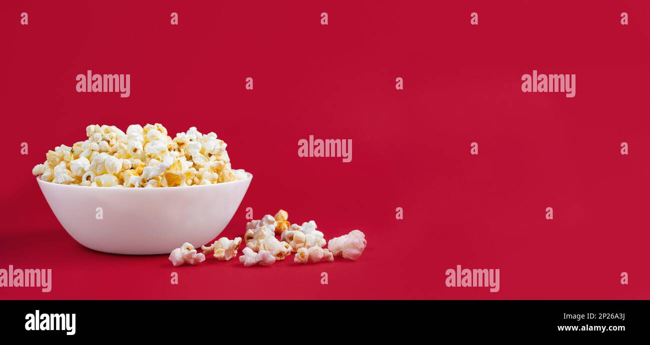 Formaggio saporito popcorn sparso in ciotola isolato su sfondo rosso. Sfondo, banner, intestazione con spazio di copia per il testo Foto Stock
