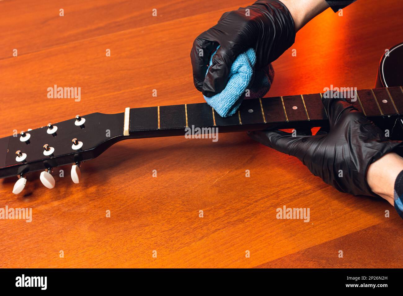 l'uomo con una chitarra, le mani di un maestro in guanti con una classica tastiera per chitarra, legno rosso nero, pulisce con un mezzo di restartboard nel wo Foto Stock