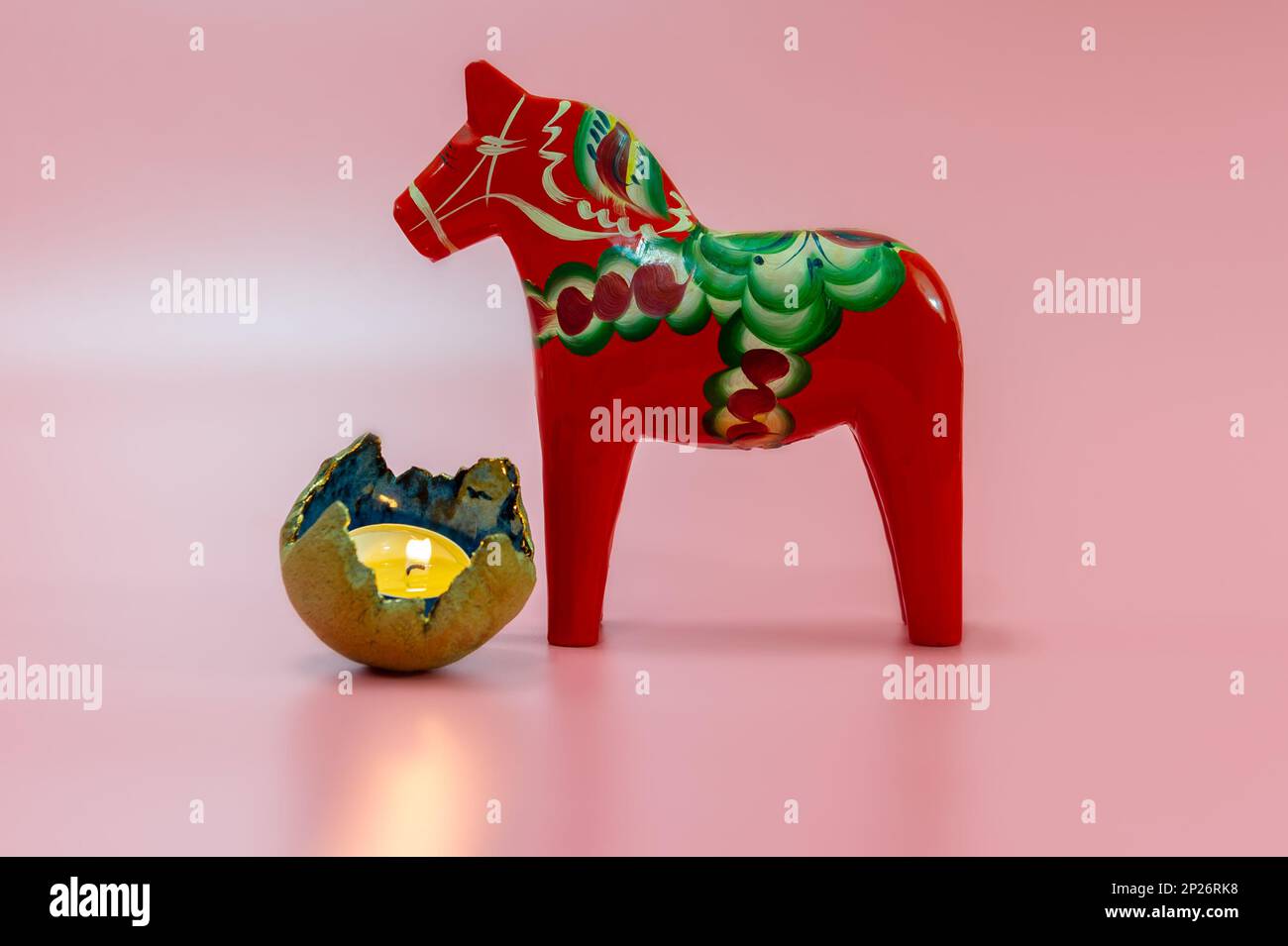 Una scena natalizia scandinava con un Cavallo di legno di Dala rosso svedese e una candela illuminata su uno sfondo rosa Foto Stock