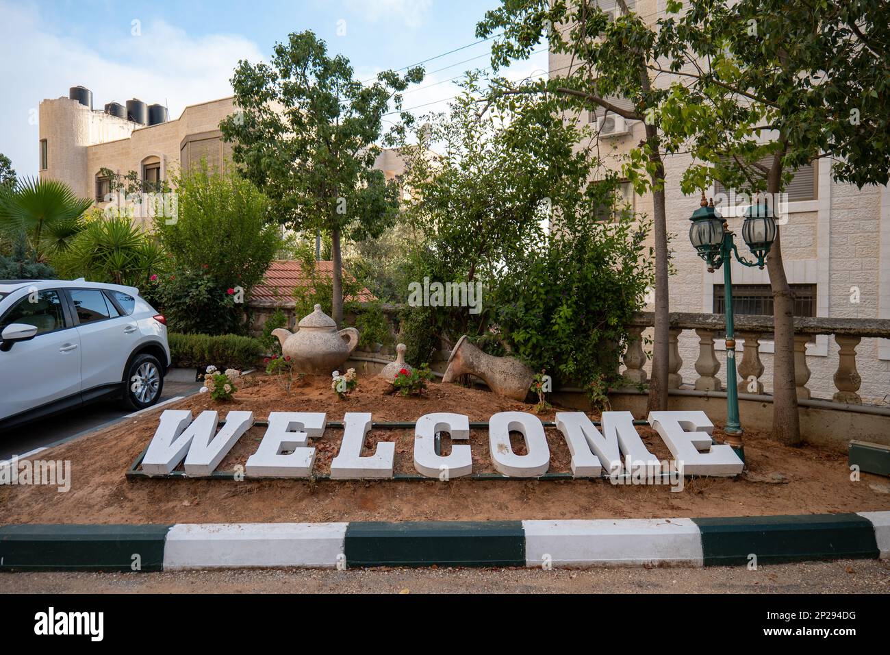White Sign in Parcheggio a Ramallah che legge 'Benvenuti' da vari alberi e una macchina bianca Foto Stock