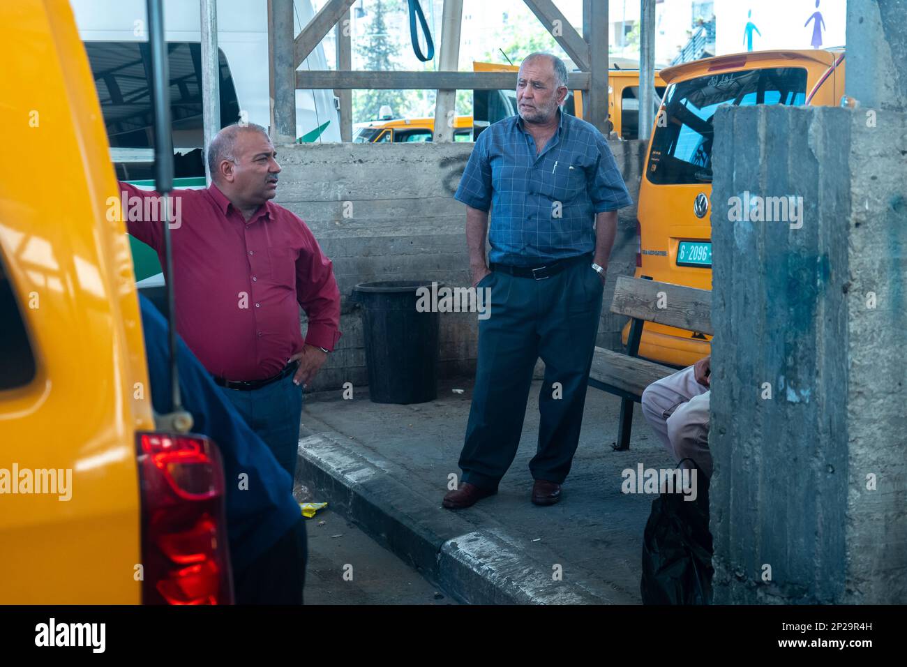 Betlemme, Cisgiordania, Palestina - 22 luglio 2022: Due lavoratori arabi maschi in Break stare in un parcheggio da Mini autobus gialli parcheggiati Foto Stock