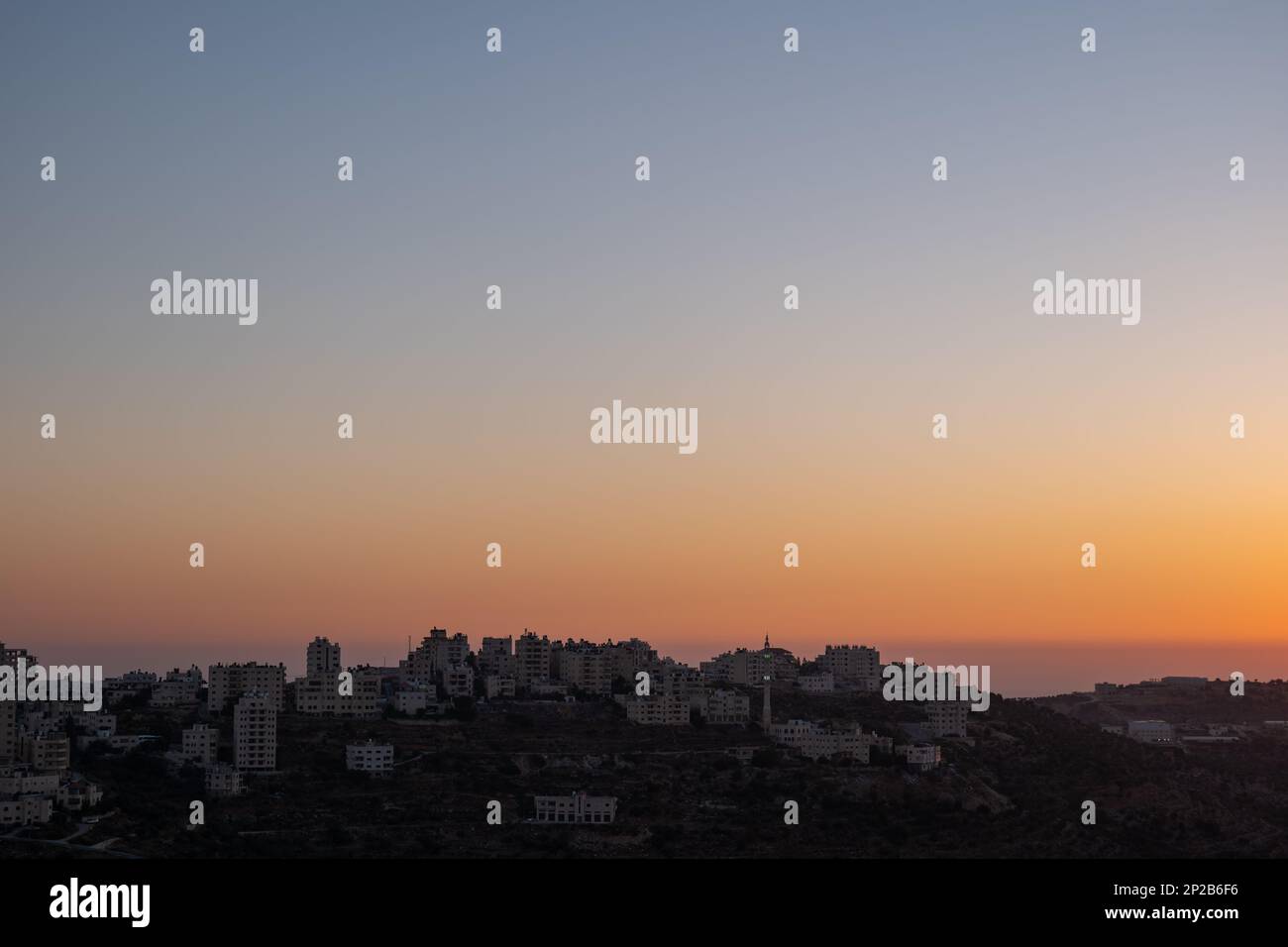 Vista panoramica scura della Città Araba di Ramallah edificio Silhouettes su una collina lontano in un deserto contro il cielo crepuscolo chiaro e colorato Foto Stock