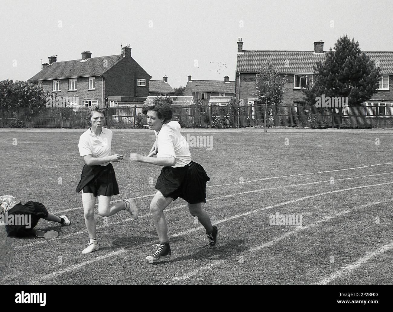 1989, al giorno degli sport della scuola secondaria, fuori su una pista d'erba, ragazze anziane che prendono parte ad una corsa di relè, una è caduta, Inghilterra, Regno Unito Foto Stock