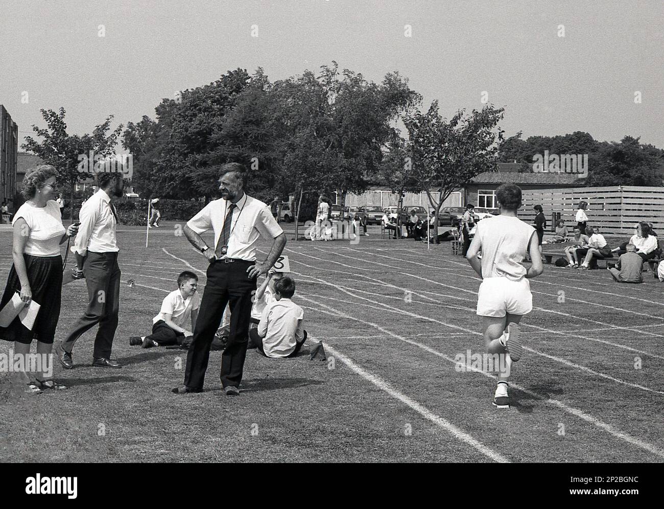1989, giornata di sport scolastici in una scuola secondaria, un ragazzo di scuola adolescente maschile che gareggia in una corsa in erba con una signora insegnante in piedi accanto, contando i giri, Sleaford, Inghilterra, Regno Unito. Foto Stock