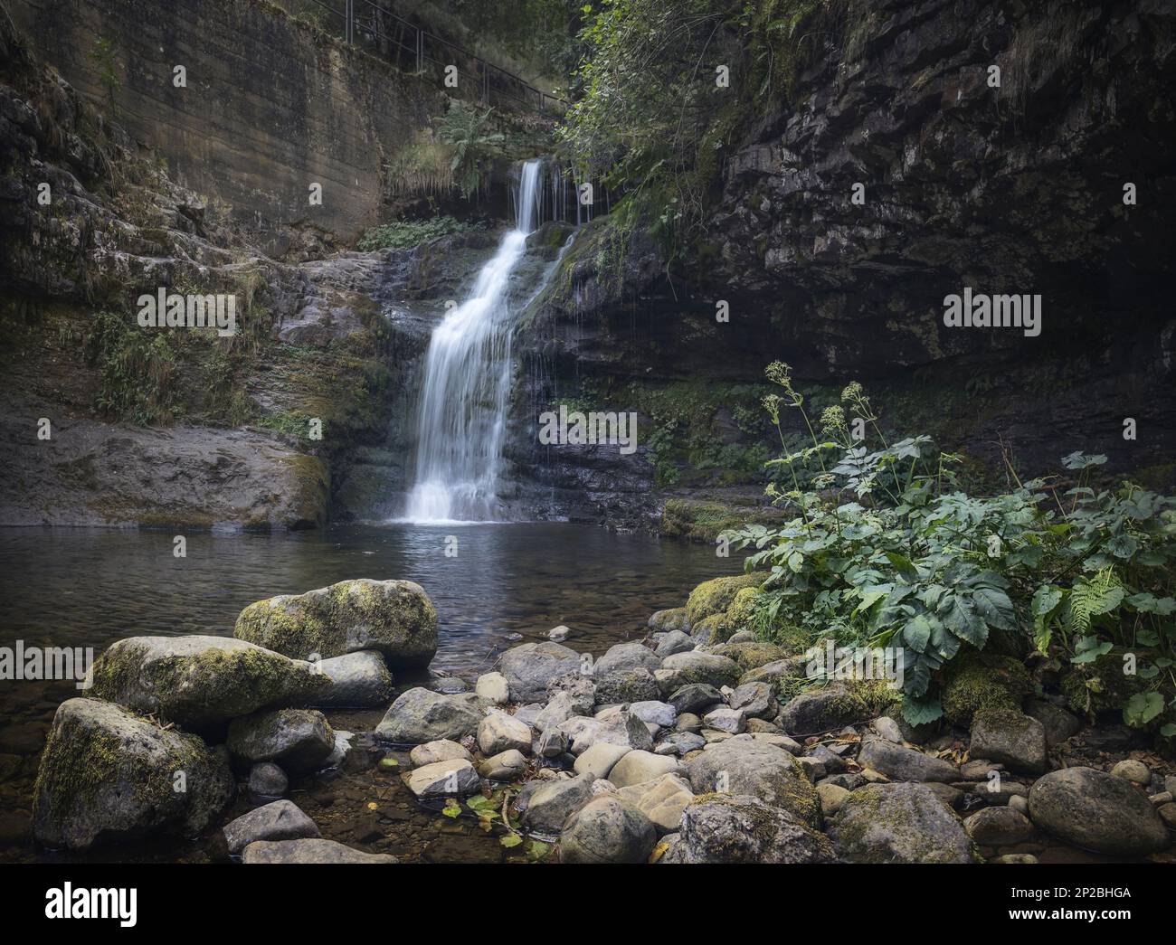 La bellezza della natura prende vita in questo lungo scatto di esposizione, con il movimento di una cascata che si sovrappone a formazioni rocciose circondate da una lussureggiante foresta Foto Stock