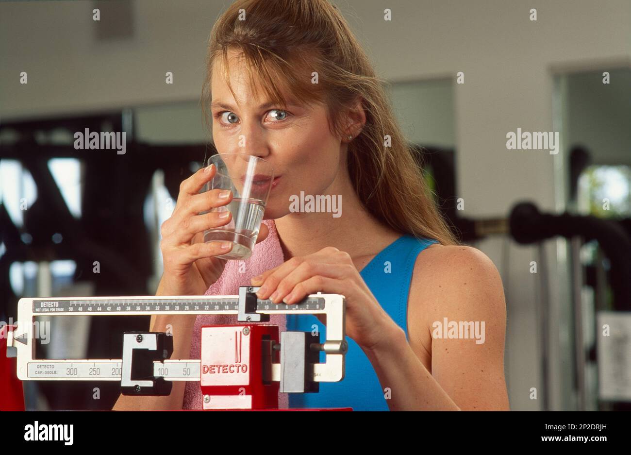 Donna giovane in palestra, prendendo un bicchiere d'acqua mentre si è in piedi su una bilancia Foto Stock