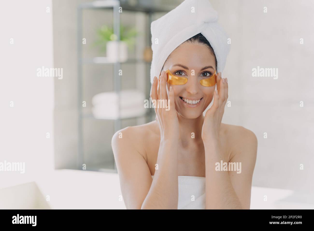 Donna che applica idrogel anti rughe dorato sotto gli occhi cerotti per una pelle sana lisciante dopo la doccia, facendo la routine mattutina cura della pelle in ba Foto Stock