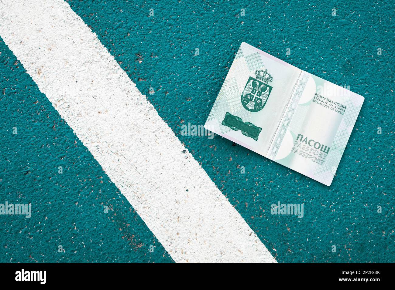 Aprire il passaporto nazionale serbo accanto a una linea bianca sul terreno. Simbolico, confine Foto Stock