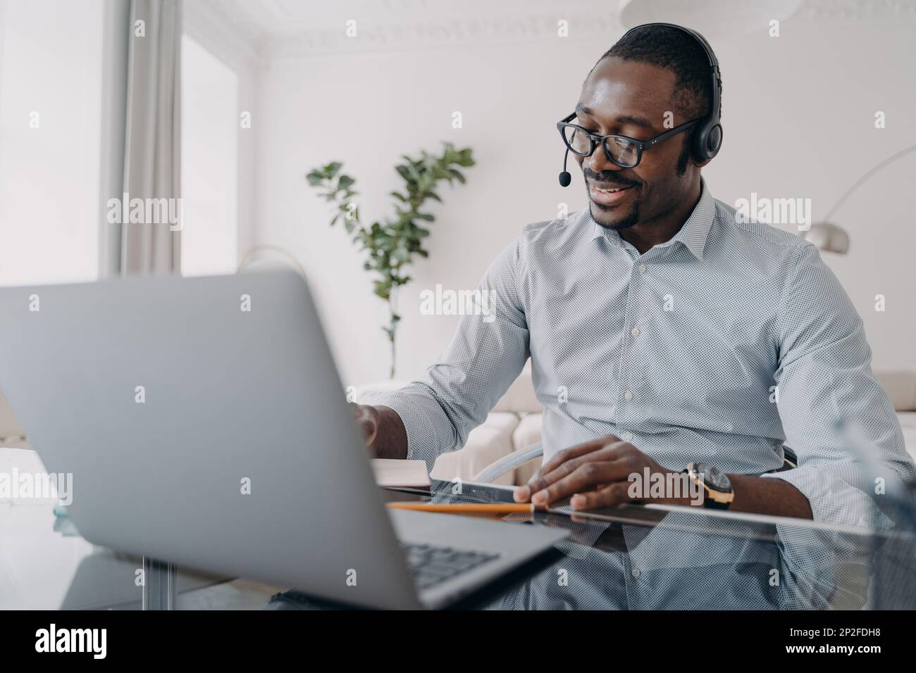 Colloquio di affari online. Il ragazzo afro-americano sta parlando davanti alla macchina fotografica. Uomo d'affari felice in abbigliamento formale e cuffie ha riunione on-line in zoom. Manag Foto Stock