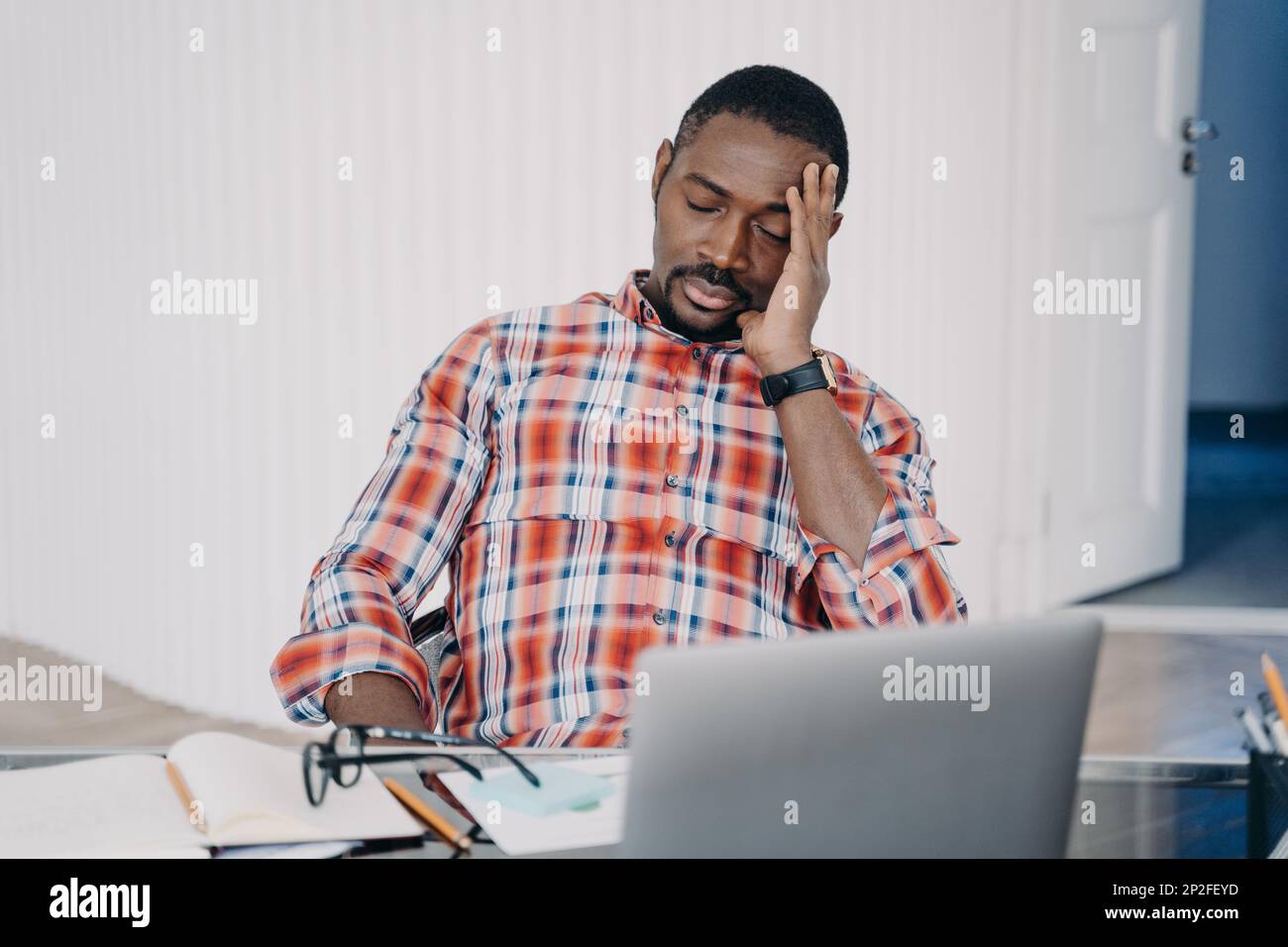 Sonnolenza stanco insegnante online ottiene mal di testa. Afro man ha una conferenza online o lavora su un computer portatile. Uomo d'affari che parla con il cliente. Dipendente occupato con proj Foto Stock