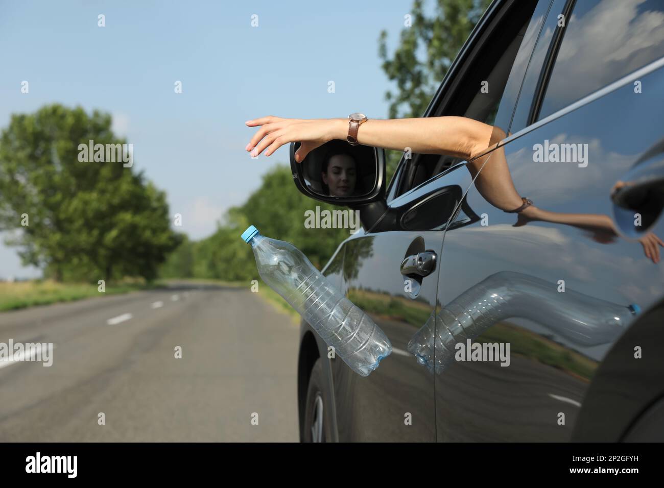 Il conducente getta via la bottiglia di plastica dal finestrino dell'auto. Spazzatura su strada Foto Stock