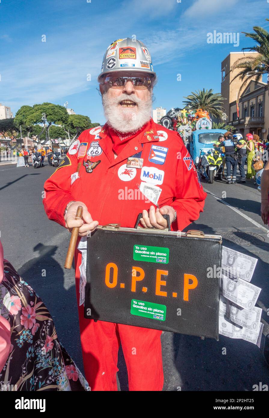 Uomo in abito di fantasia al Carnevale di Las Palmas vestito in rosso tuta e trasporto OPEC valigetta piena di dollari. Profitti dell'industria petrolifera, bonus, bonus, riscaldamento globale... concetto Foto Stock