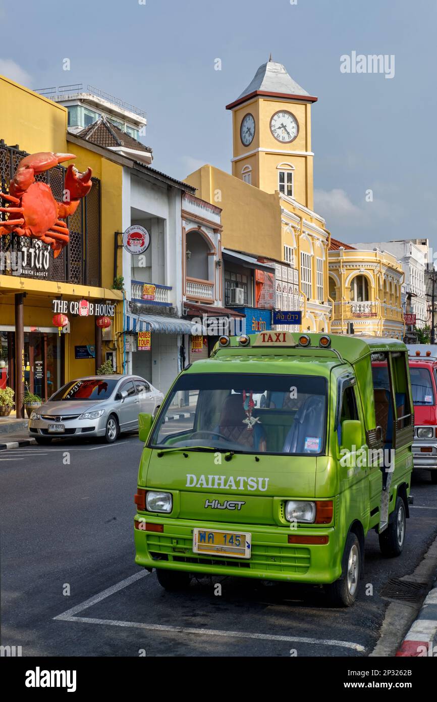 Un pittoresco songthaew blu-giallo, un tipo di autobus locale, passando il simbolo della torre dell'orologio nella zona della Città Vecchia di Phuket (Phuket City), Thailandia Foto Stock