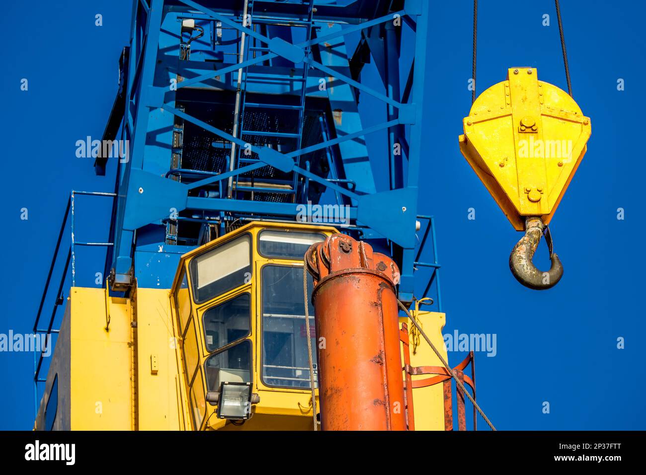 Cabina gialla di gru di cantiere in vista frontale ravvicinata, con gancio davanti al cielo azzurro, che evocano potenza ed efficienza. Foto Stock
