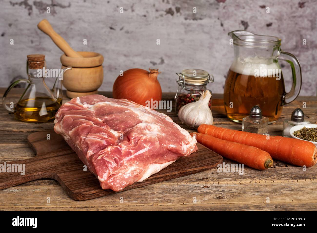Un pezzo di lombo di maiale con carote, birra, cipolla, aglio ed erbe aromatiche, preparazioni per preparare un delizioso piatto in pentola. Foto Stock