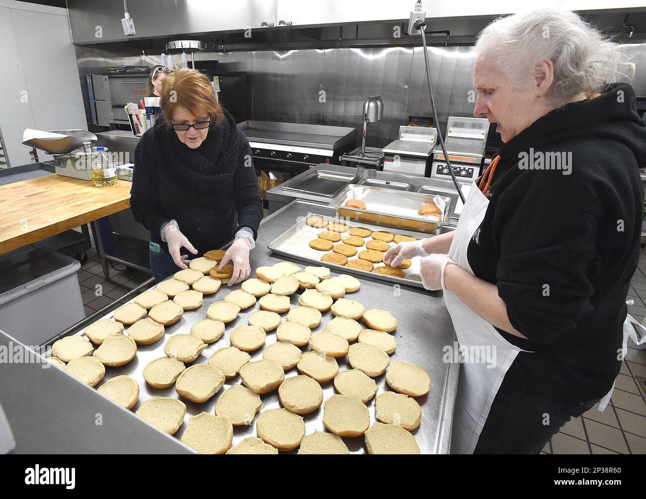 Food Service employees Jeanne Lovelace, left, and Joanne Hayes prepare chicken sandwiches for South Albany High School at the Linn County Fairgrounds in Albany, Ore., Monday, April 6, 2015. Five days after an arson fire burned down the cafeteria, students at the school were back in class Monday, with a makeshift lunchroom in the gym and what the principal called a "very aggressive schedule" for rebuilding. (AP Photo/Albany Democrat-Herald, Mark Ylen) Foto Stock