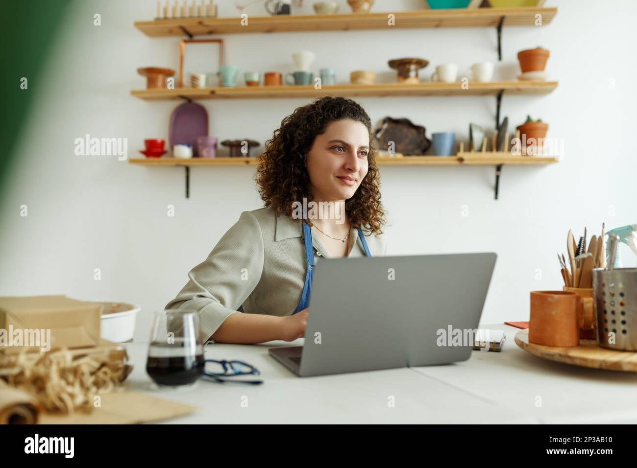 Imprenditore Potter che usa il laptop in officina, sorridendo Foto Stock