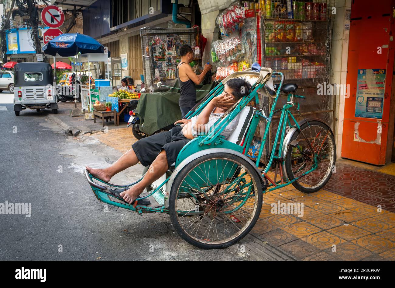 Un conducente di ciclo tradizionale ha un sonno nel suo pedicab lungo una strada laterale a Phnom Penh, Cambogia. Foto Stock