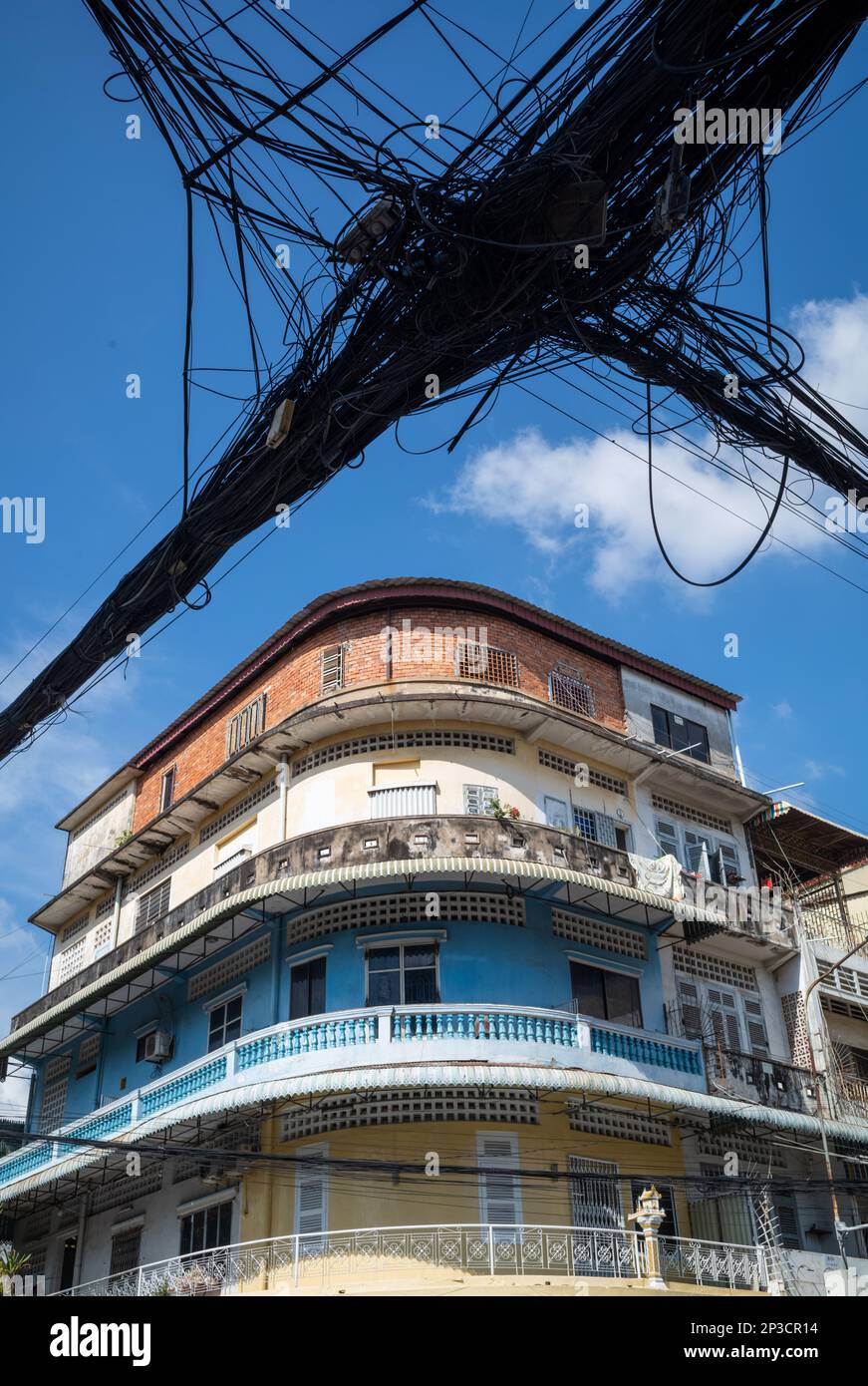 Una massa di cavi telefonici e di alimentazione appendono accanto ad un vecchio edificio di appartamenti nel centro di Phnom Penh, Cambogia. Foto Stock