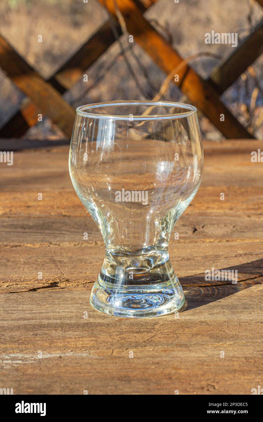 Un bicchiere vuoto, su un tavolo di legno in un gazebo, ai raggi del sole. Foto Stock