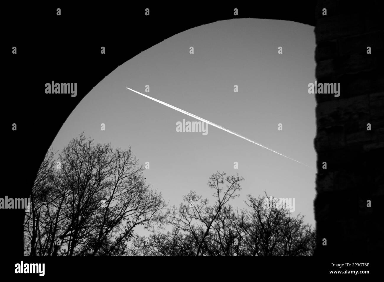 Vista del cielo al tramonto sotto un ponte come un aereo vola in alto lasciando un contrail / percorso vapore / percorso vapore / contraglie nel cielo Foto Stock