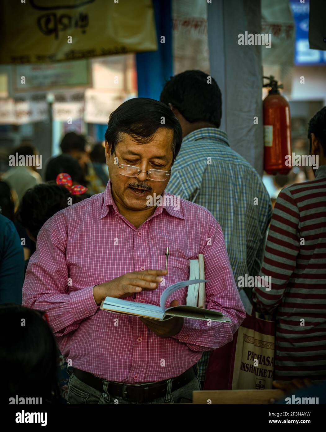 Kolkata, India - 12 febbraio 2023: Un uomo si è ingenuato a leggere un libro in mezzo alla folla vibrante alla Fiera del Libro di Kolkata. Messa a fuoco selettiva. Foto Stock