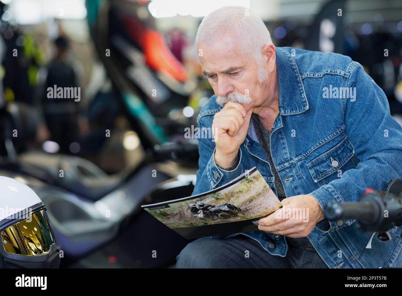 uomo anziano che guarda la brochure del veicolo nello showroom Foto Stock