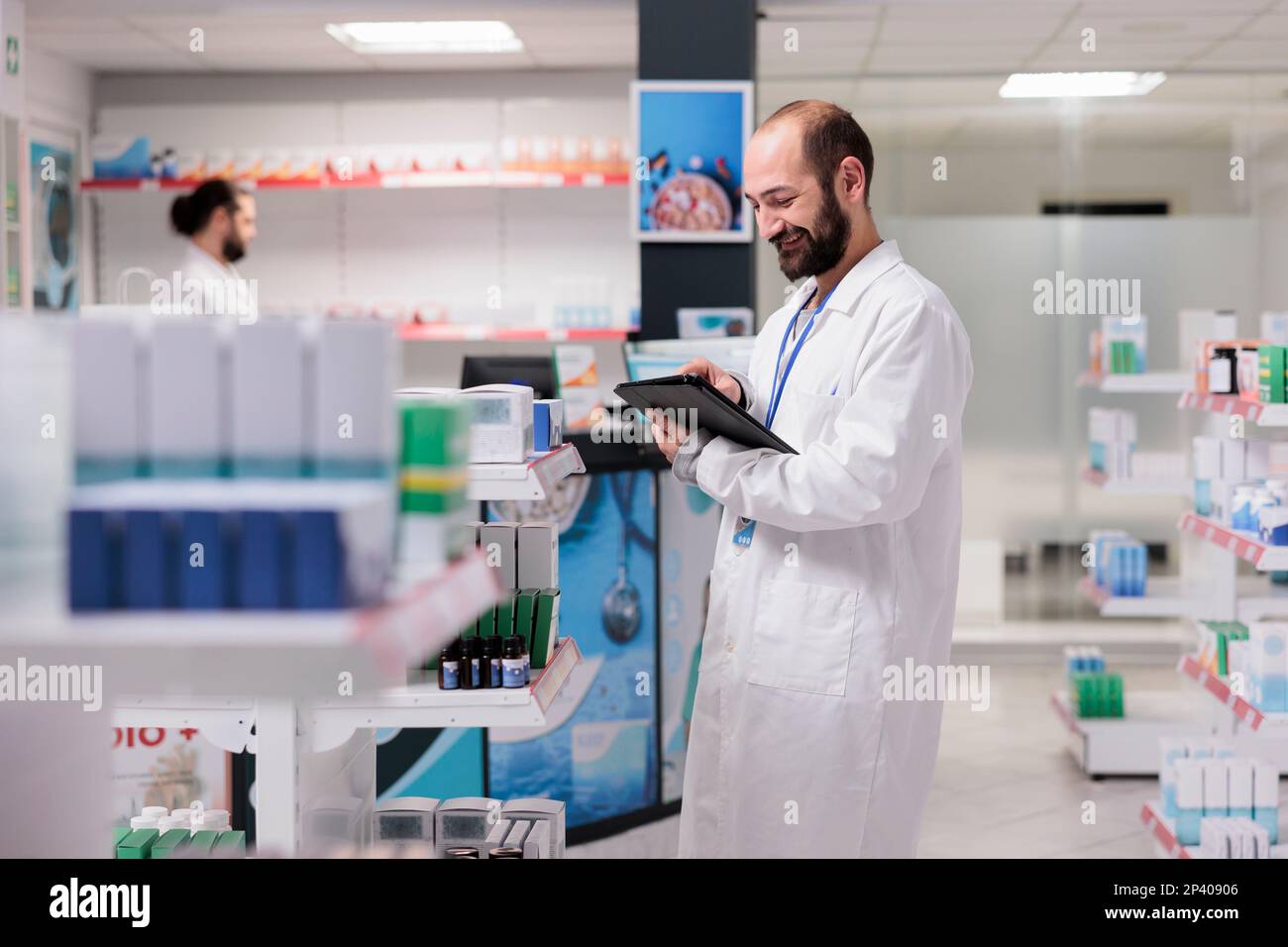 Dipendente farmacia che tiene il computer tablet controllo prescrizione del cliente durante la preparazione di pillole ordine. Farmacia mantiene un inventario di tutti i diversi tipi di pillole e forniture mediche in magazzino. Foto Stock