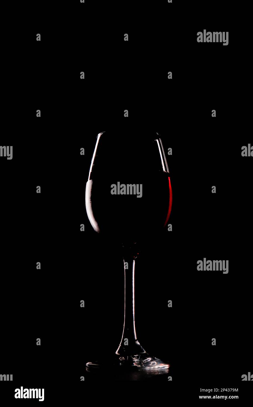 Un vino rosso ricco e vellutato in un vetro delicato e dal design intricato, con la silhouette che accentua gli intricati dettagli della vetreria. Foto Stock