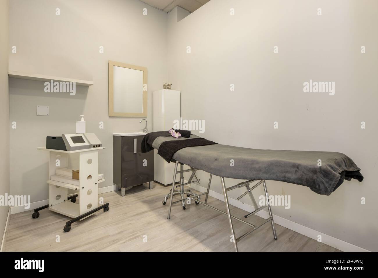Cabina di trattamento in una clinica di bellezza con dispositivi elettronici per l'applicazione di massaggi terapeutici, barella con copertura grigia e lavello con mirr Foto Stock