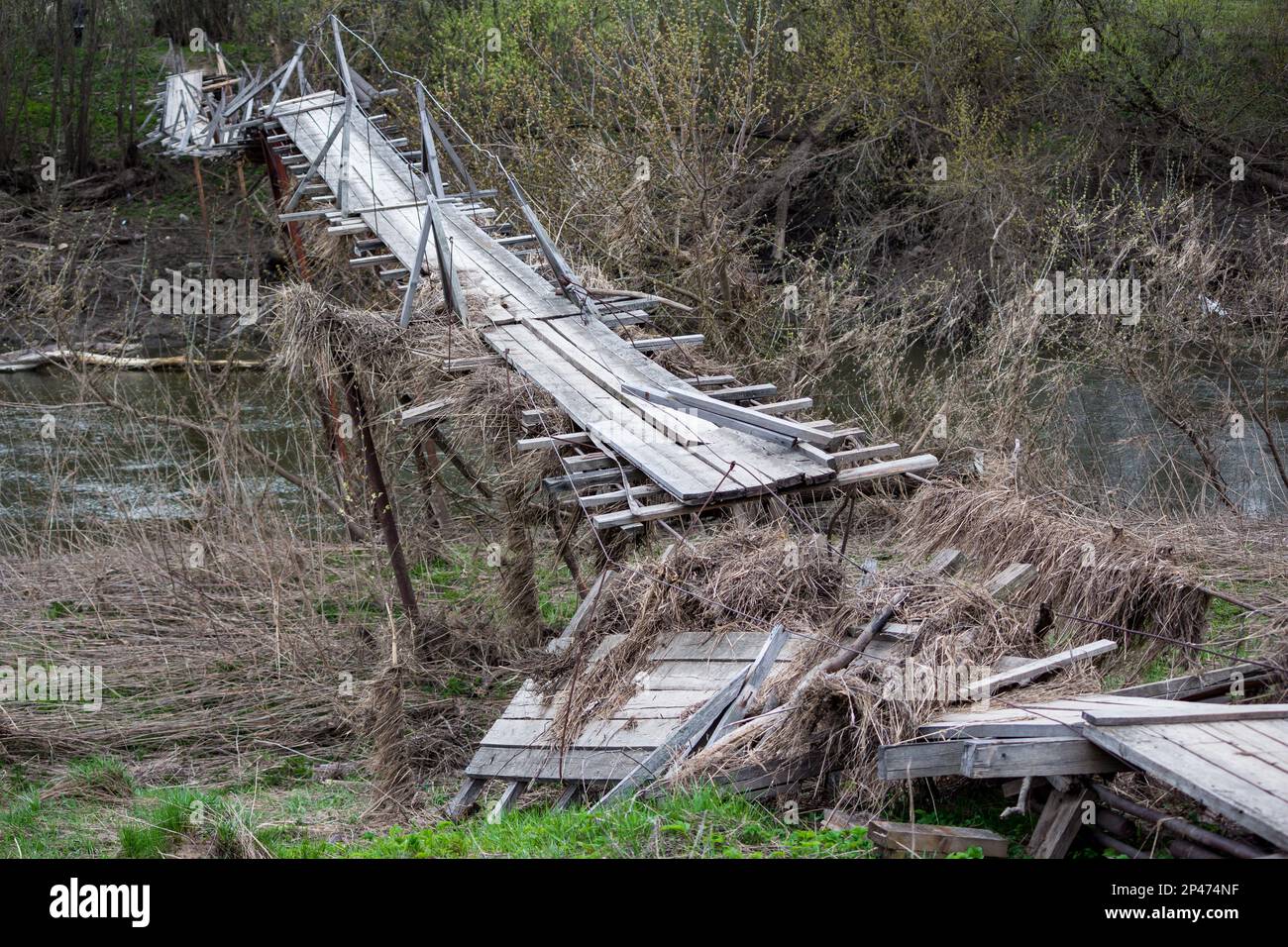 Ponte pedonale rotto e inclinato dopo una pesante alluvione su un fiume in campagna Foto Stock