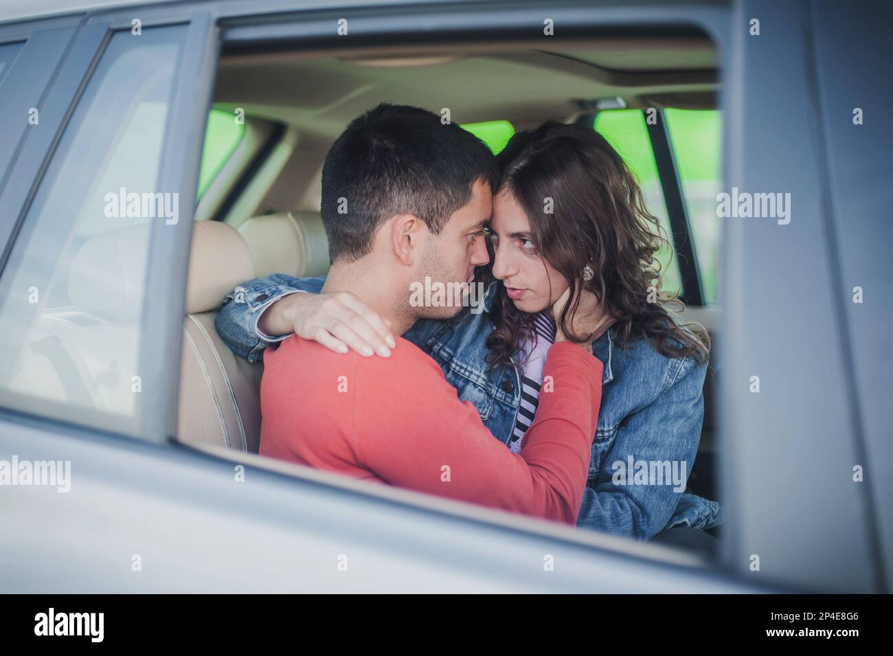 Bacio appassionato in auto. Visualizza attraverso la finestra. Giovane coppia sexy innamorata, seduta sul sedile posteriore, guardando e baciandosi appassionatamente l'un l'altro, jus Foto Stock