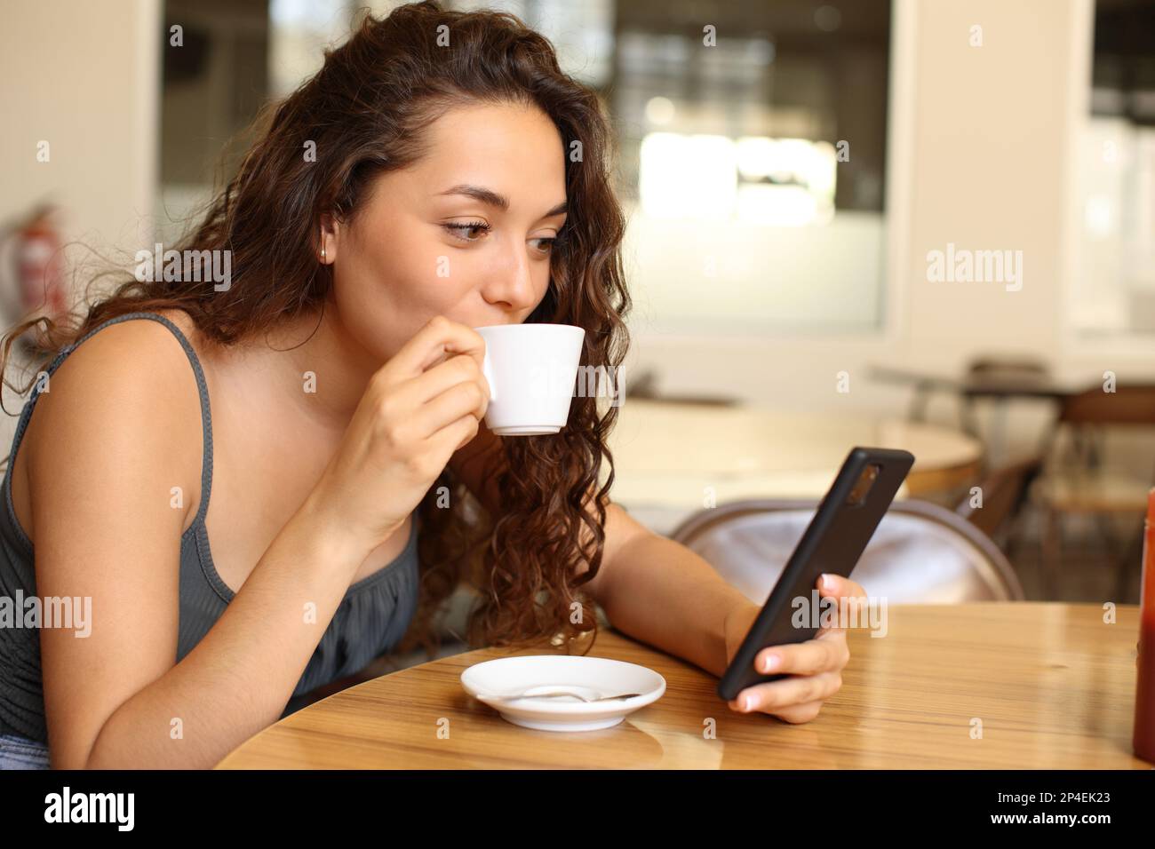 Donna in un ristorante bere caffè e controllare lo smartphone Foto Stock