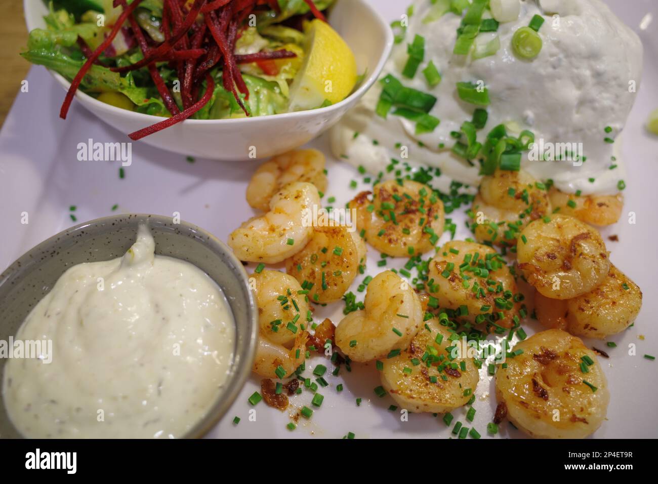 i gamberetti appena fritti sono disposti su un piatto con salsa all'aglio e insalata Foto Stock